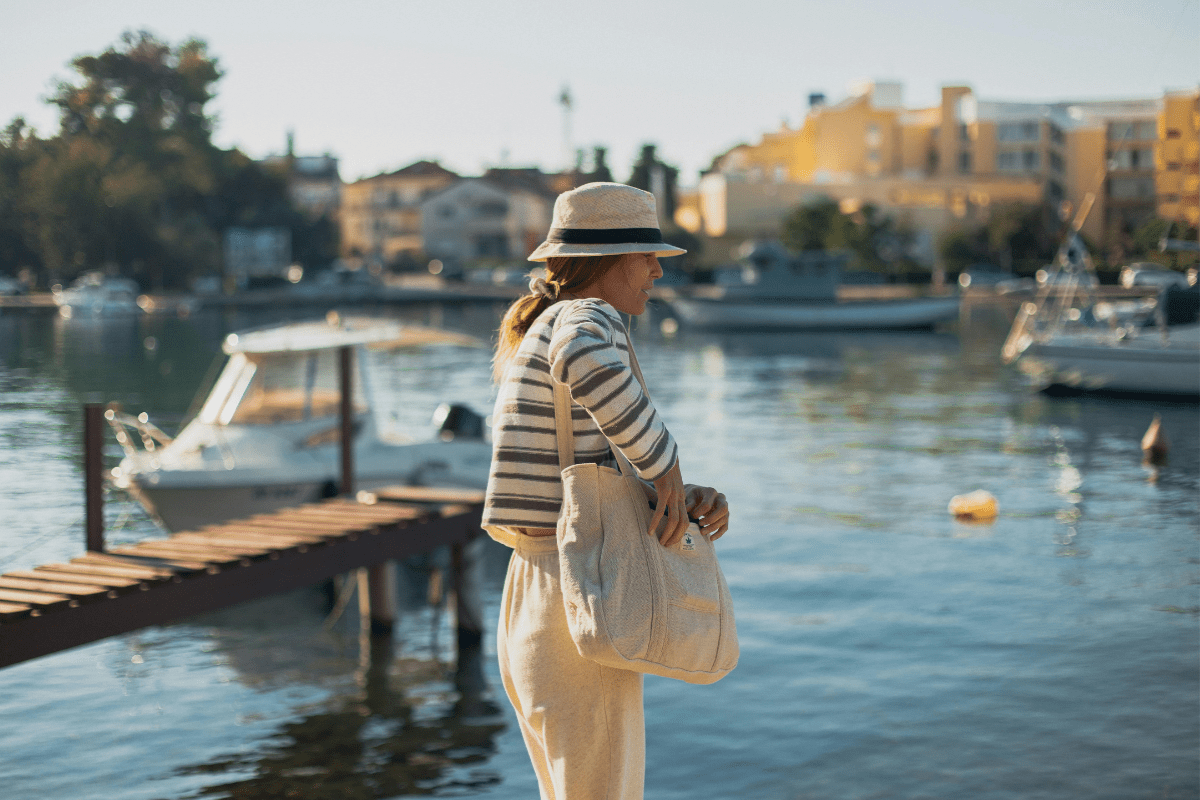 Leben in Kroatien – Frau mit Strohhut am Hafen, Boote und mediterrane Häuser im Hintergrund.